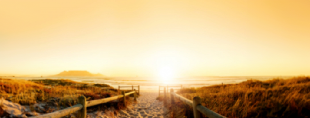 Strandweg mit Holzgeländern zum Meer bei Sonnenuntergang – ruhige, tröstliche Stimmung.