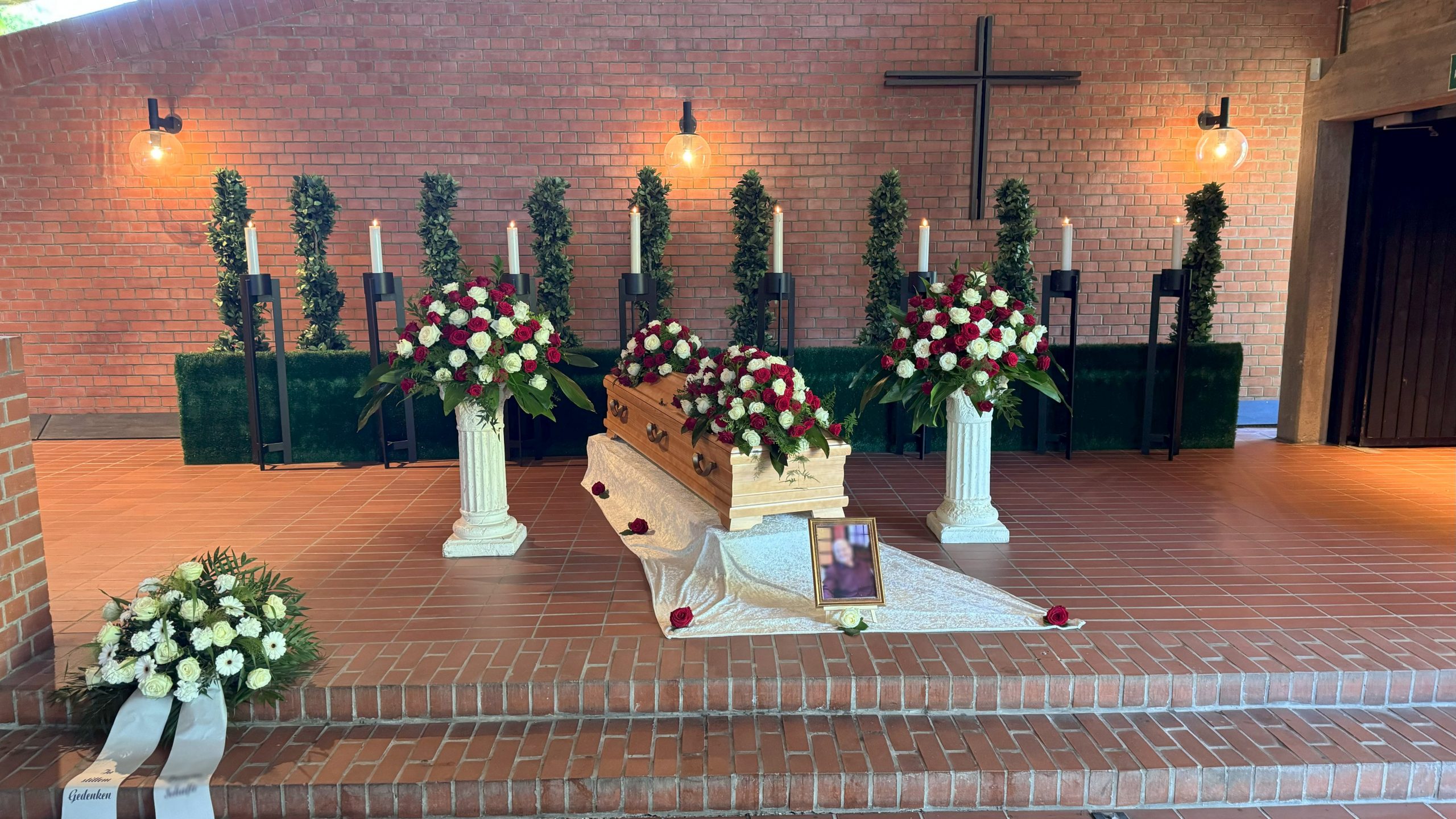 Trauerfeier in der Kapelle in Laatzen: Holzsarg mit roten und weißen Rosen, feierlich geschmückt mit Kerzen und Blumenarrangements.